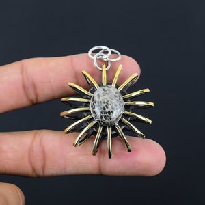 May include: A silver and gold pendant featuring a fossilized stone in the center, surrounded by a sunburst design.