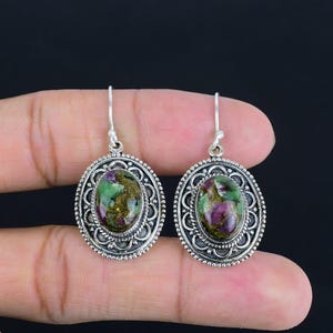 May include: A pair of silver earrings featuring oval green and pink gemstone cabochons set in ornate silver frames.
