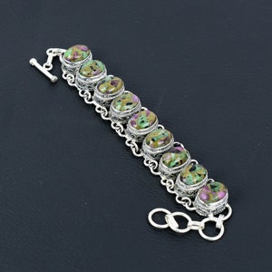 May include: A silver bracelet with a chain link design and oval-shaped green, pink, and black gemstones.