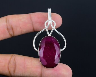 Può includere: Un ciondolo in argento con una grande pietra di rubino ovale sfaccettata. Il ciondolo ha un design delicato e traforato con due anelli a forma di cuore.