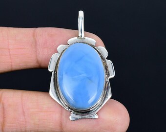 May include: A silver pendant featuring a large, oval-shaped, light blue gemstone. The gemstone is set in a decorative silver frame with a loop at the top for a chain. The pendant is held in a hand against a black background.