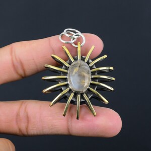 May include: A silver and gold pendant with a sunburst design. The pendant features a central oval-shaped stone surrounded by gold rays and a silver frame. The pendant is suspended from a silver bail.