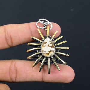 May include: A brass and silver pendant with a white and brown shell inlay. The pendant is shaped like a sun with rays extending from the center. The shell inlay is in the center of the pendant and is surrounded by a silver ring.
