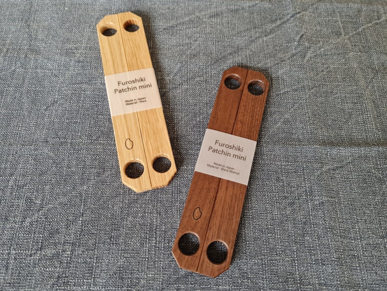 Zu sehen sind zwei Furoshiki-Holzgriffe, auch Patchin genannt. Der linke ist aus hellem Eichenholz gefertigt, der rechte aus dunklem Walnussholz.