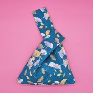 May include: A teal blue fabric tote bag with a white and yellow ginkgo leaf pattern. The bag is folded into a triangular shape.