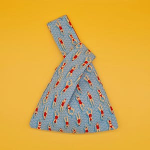 May include: A blue fabric tote bag with a pattern of swimmers in red and white bathing suits. The bag is folded and tied in a knot.
