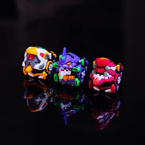 May include: Three colorful, stylized robot figurines. The robots are in yellow, white, red, purple, and green. The figurines are on a reflective black surface.
