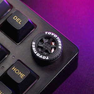 May include: Black keyboard keycap with a black tyre design and white "TOYO TIRES" lettering.