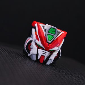 May include: A red, white, and green robot head with a detailed design. The robot head has a green visor and a red mouth.