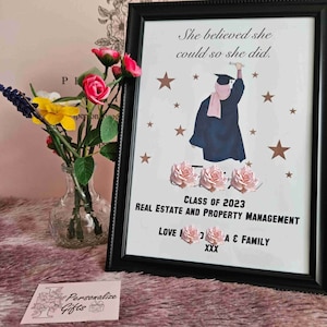 May include: A framed graduation print with a gold background and stars. The print features a silhouette of a person in a graduation cap and gown reaching for a star. The text reads "She believed she could so she did."  "Class of 2023"  "Real Estate and Property Management"  "Love [Name] A & Family"  "XXX"
