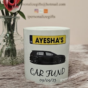 May include: White ceramic money box with a black car illustration and the text "Ayesha's Car Fund 09/09/23".
