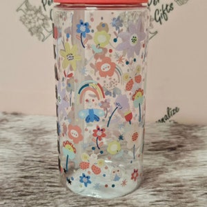Peut inclure: Une bouteille d'eau en plastique transparent avec un couvercle rose et une paille. La bouteille est d&eacute;cor&eacute;e d'un motif color&eacute; de papillons, de fleurs et d'arcs-en-ciel.