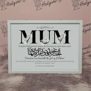 Puede incluir: Un estampado enmarcado con la palabra "MUM" en letras negras grandes, decorado con detalles florales. El estampado incluye una cita en árabe e inglés, con el texto "El paraíso está bajo los pies de las madres."