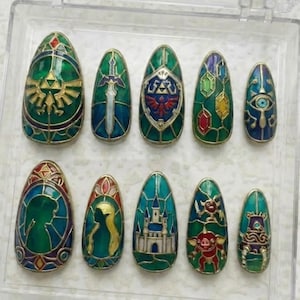Könnte beinhalten: Ein Set aus zehn ovalen Kunstnägeln mit aufwendigen Designs im Stil von Glasmalereien. Die Nägel zeigen verschiedene Symbole und Charaktere, darunter ein Schwert, ein Schild und ein Schloss, in Grün-, Gold- und Blautönen, in einer transparenten Kunststoffbox.