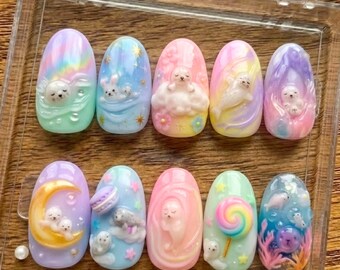 May include: A set of ten oval-shaped press-on nails in a clear plastic case. Each nail features a unique design with pastel colors, including seals, rainbows, clouds, and a lollipop. The nails are a mix of pink, blue, yellow, and purple.