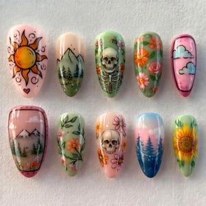 Könnte beinhalten: Ein Satz von zehn bemalten Kunstnägeln mit verschiedenen Designs. Die Designs umfassen eine Sonne, Berge, Blumen, einen Totenkopf, Wolken und eine Sonnenblume. Die Nägel sind in einer Vielzahl von Farben bemalt, darunter Rosa, Grün, Orange und Blau.