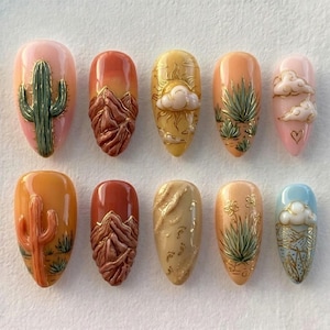 Könnte beinhalten: Ein Set von zehn mandelförmigen Acrylnägeln mit Designs zum Thema Wüste. Jeder Nagel zeigt ein anderes Design, darunter Kakteen, Berge, Wolken und Wüstenpflanzen, in Orange-, Rosa-, Gelb- und Grüntönen. Einige Nägel haben goldene Akzente.