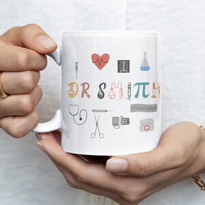May include: White ceramic mug with a colorful design featuring medical symbols and the text "I &hearts; DR SMITH".