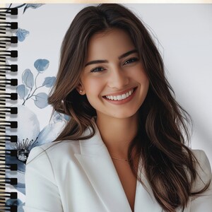 May include: A white spiral bound notebook with a floral design featuring blue and white flowers. The notebook has a black binding and is closed.