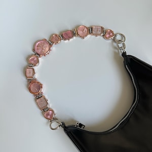 May include: A black leather handbag with a pink and gold watch chain strap. The strap is made of multiple small watches and heart-shaped charms.