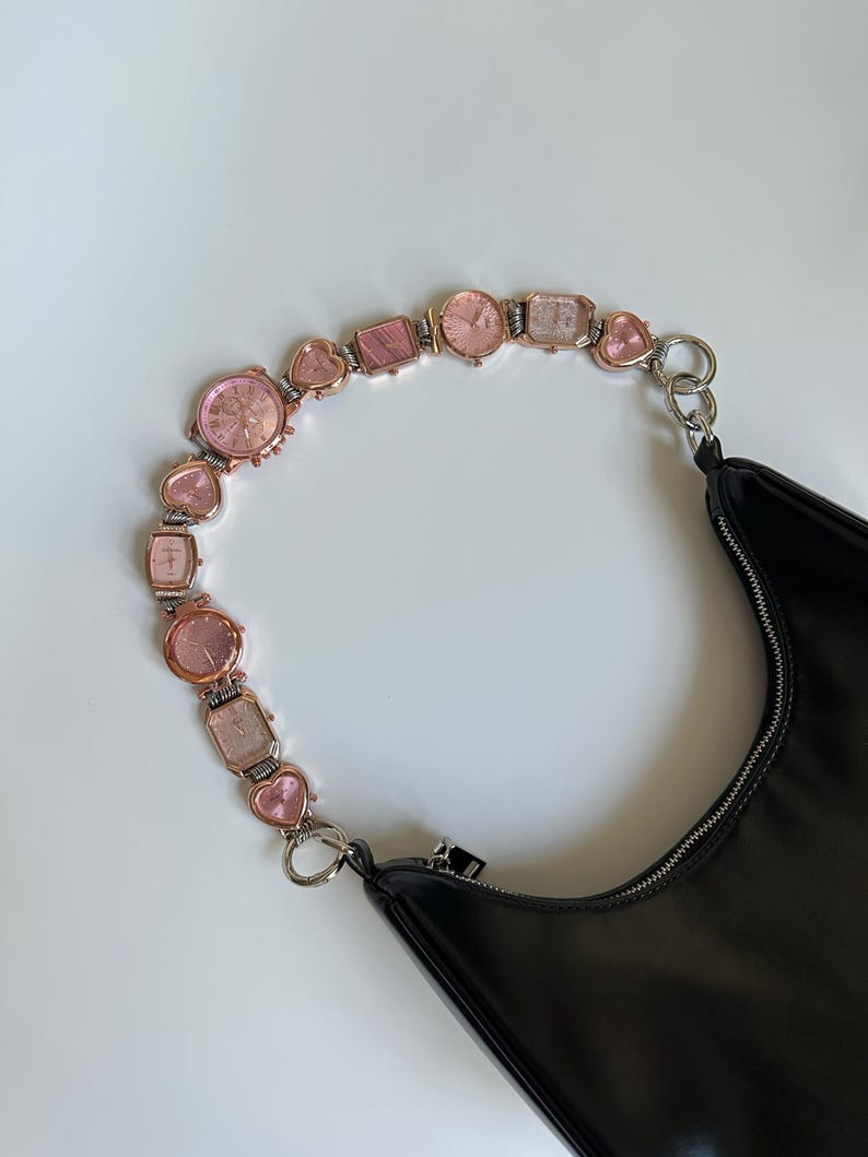 May include: A black leather handbag with a pink and gold watch chain strap. The strap is made of multiple small watches and heart-shaped charms.