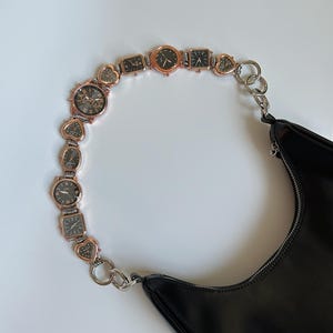 May include: A black leather handbag with a chain strap made of linked watch faces. The strap is silver and gold toned.
