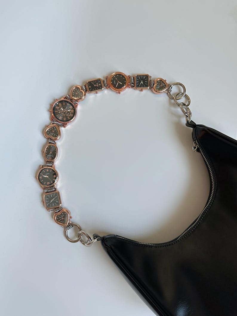 May include: A black leather handbag with a chain strap made of linked watch faces. The strap is silver and gold toned.