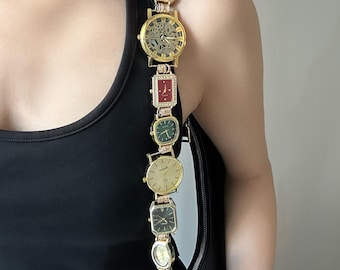 May include: A unique gold-toned watch strap featuring a variety of watch faces in different shapes and colors. The strap is attached to a black bag with a silver zipper. The watches include green, red, and gold faces.