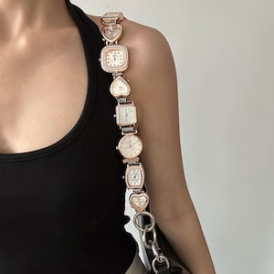 May include: A gold-tone chain bag strap with multiple small watch faces attached. The strap is made up of linked hearts and square watch faces.