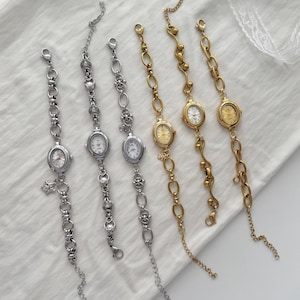 Könnte beinhalten: Sechs zarte Armbanduhren mit ovalen Zifferblättern und Kettengliederbändern. Drei sind silberfarben und drei goldfarben. Die Zifferblätter der Uhren haben römische Ziffern. Die Uhren werden auf einer weißen Oberfläche präsentiert.