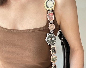 May include: A brown tank top with a silver chain strap with multiple watch faces attached. The strap is worn over the shoulder and has a black handbag attached to it.