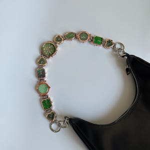 May include: A black leather handbag with a chain strap made of multiple small green and gold watches.