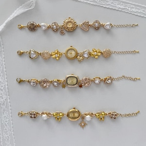 May include: Four gold-coloured watch bracelets with decorative elements. Each bracelet has a watch face and is adorned with pearls, hearts, flowers, and charms. The bracelets are displayed on a white surface.