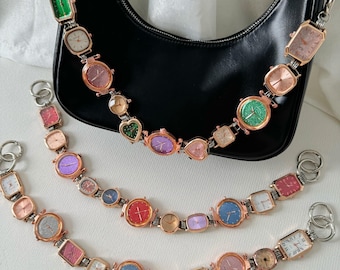 Könnte beinhalten: Eine schwarze Ledertasche mit einer Kettenkette, die mit einer Reihe von bunten Armbanduhren verziert ist. Die Uhren sind mit Metallgliedern an der Kette befestigt und haben verschiedene farbige Zifferblätter und Zeiger.