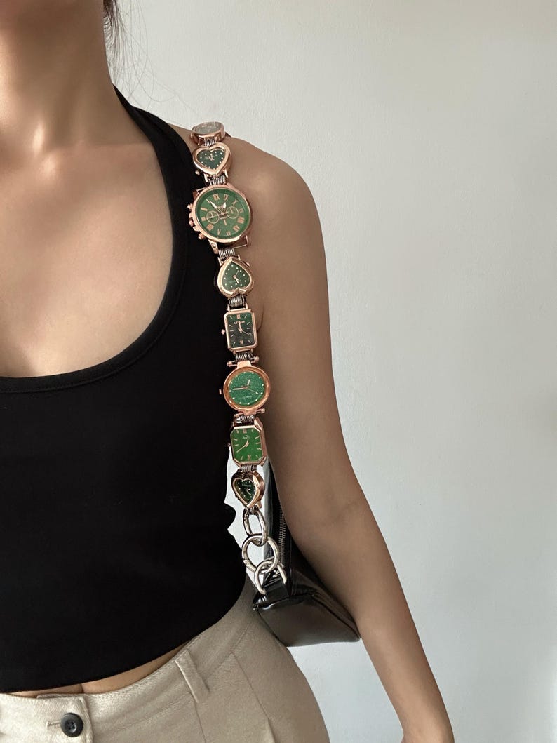 May include: A gold chain strap with multiple green and gold watches attached. The strap is worn over a black tank top and beige pants.