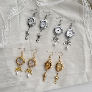 May include: A collection of vintage-style earrings featuring miniature watch faces. The earrings are available in silver and gold tones, with designs including star and bow accents, and faux pearls. The watch faces have white dials and black numerals.