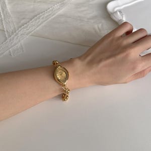 May include: A gold-toned wristwatch with an oval face and a linked bracelet. The watch has a gold dial and is worn on a wrist. The watch is a classic accessory.