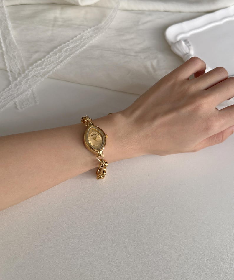May include: A gold-toned wristwatch with an oval face and a linked bracelet. The watch has a gold dial and is worn on a wrist. The watch is a classic accessory.