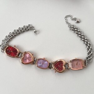 May include: A silver chain bracelet with four heart-shaped watches. The watches have different colored faces: red, pink, purple, and gold.