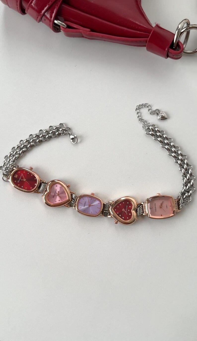 May include: A silver chain bracelet with four heart-shaped watches. The watches have different colored faces: red, pink, purple, and gold.