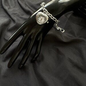 May include: A silver heart-shaped watch with a chain bracelet. The watch face has black numbers and hands.