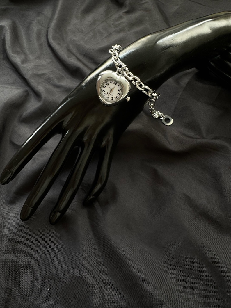 May include: A silver heart-shaped watch with a chain bracelet. The watch face has black numbers and hands.