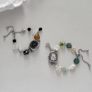 May include: Two decorative wristwatches with silver-toned metal bands. One watch has a black face and the other has a white face. Both watches are adorned with colorful beads and floral accents.