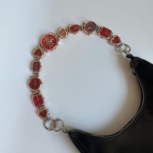 May include: A black leather handbag with a chain strap made of linked watches with red and gold accents.