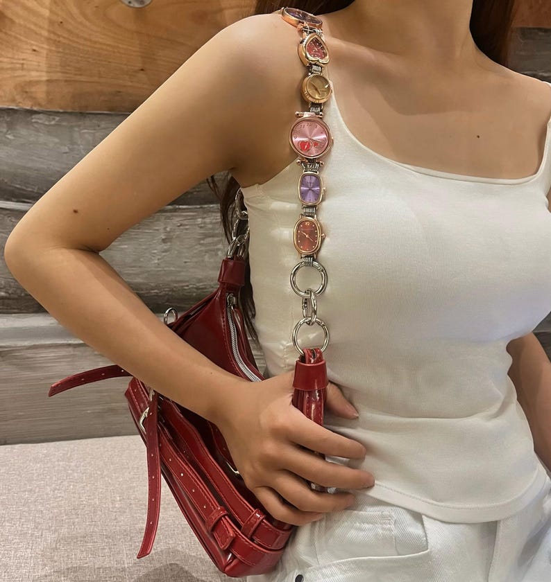 May include: A red leather shoulder bag with a chain strap featuring multiple colorful watch faces.