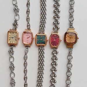 Könnte beinhalten: Fünf silberne Armbanduhren mit verschiedenen Zifferblättern und Armband-Stilen. Die Uhren haben quadratische und ovale Zifferblätter mit römischen und arabischen Ziffern. Die Armbänder sind aus verschiedenen Arten von verlinktem Metall gefertigt.