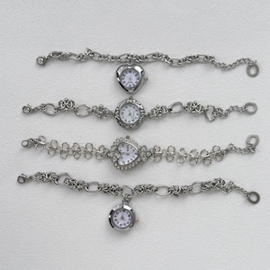 May include: Four silver wristwatches with different styles of bands and face designs. The watches have white faces with black numbers and hands.
