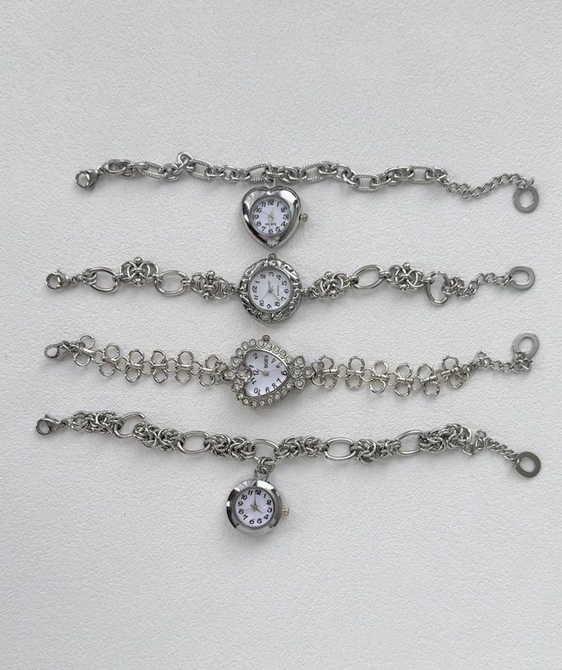 May include: Four silver wristwatches with different styles of bands and face designs. The watches have white faces with black numbers and hands.