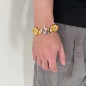 May include: A gold-toned watch bracelet with multiple watch faces. The watch faces are all different sizes and shapes. The bracelet is worn on a person's wrist.