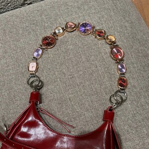 May include: A red leather handbag with a strap made of a chain of small, colorful watches.